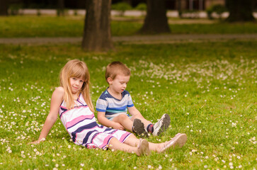 Naklejka na ściany i meble Little boy and girl playing on the meadow full of white flowers in spring