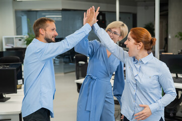 Obraz premium Colleagues give a high five in the office. Red-haired woman, blonde and bearded man in a denim shirt in the office.