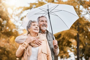 Fotobehang Senior couple, umbrella and walking outdoor for relax freedom, calm quality time and relationship bonding in summer. Elderly man, woman and wellness walk in countryside park together for love or care © C Daniels/peopleimages.com