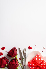 Valentine's Day concept. Top view vertical photo of bouquet of red roses dish with present box hearts knife fork and confetti on isolated white background with copyspace