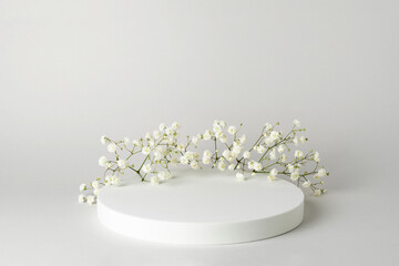 Empty white round podium and gypsophila flowers on light grey background. Showcase for product...