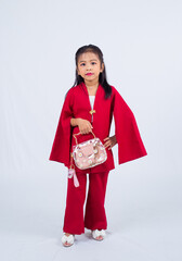Adorable 6 years old asian girl in red dress, holding a fashionable handbag in a studio isolated on white background. 