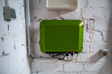 Green inverter of a photovoltaic system mounted on a white basement wall