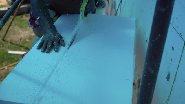 Man Cutting Polystyrene Foam Heat Insulation With Hand Saw, Closeup Detail - Everything In Blue Because Coloured Protective Foil Near