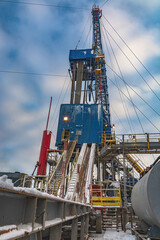Fototapeta premium Drilling rig and drilling rig equipment for drilling oil and gas wells. Winter day. Snow lies on the structures of the installation. Blue cloudy sky