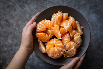 Tangerines in a bowl. The hands of a European woman hold a plate of peeled tangerines. Selective focus, dark and moody photo, shallow depth of field