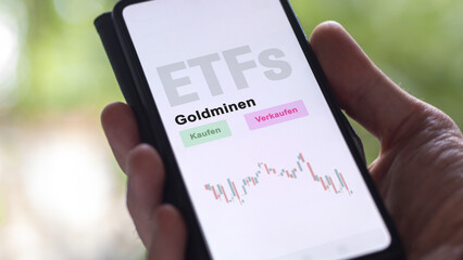 December 2022. An investor analyzes the gold mines ETF fund on phone screen Goldminen-ETFs. German text translated :Kaufen, Verkaufen, Goldminen= buy, Sell, gold mines