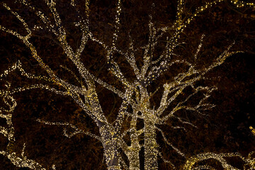 The winter tree is decorated with glowing garlands and lights, dark background, selective focus. Christmas decoration of city parks and trees.