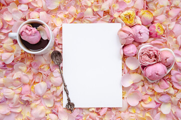 Background of pink rose buds and petals with blank card in centre and a cup of tea with rose and tea spoon. Flat lay, overhead view. Mother's Day, St. Valentine's Day, March 8 concept.