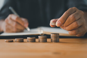 A businessman stacks coins while writing in a notebook. business success and growth. tax and financial