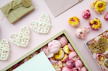 Valentine's Day composition. Flat lay of white hearts, handmade gift boxes, craft paper, envelope, rose buds on pink background. Top view, Copy space. Template postcard for holiday