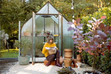 Young woman sits with basket full of tulip bulbs for planting in front of tiny glass orangery in...