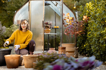 Woman planting flower bulbs in clay jugs for growing in glass orangery at garden. Florist gardening...