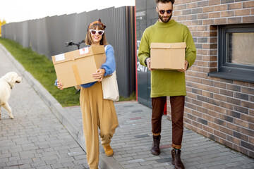 Cheerful young man and woman carry cardboard parcels together received in automatic post machine outdoors. Concept of modern delivery technologies