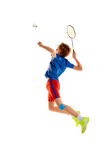 Portrait of teen boy in uniform playing badminton, serving shuttlecock with racket in a jump isolated over white background