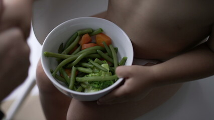 Toddler baby holding bowl of green veggies