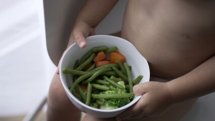 Toddler baby holding bowl of green veggies