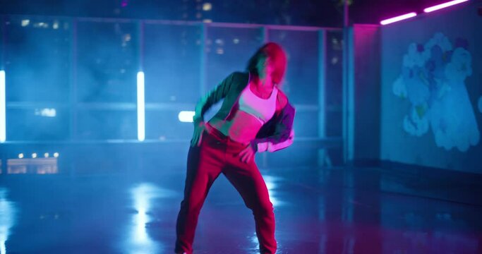 Cheerful Young Professional Woman in Athletic Attire is Dancing Energetically on an Urban Rooftop Parking Lot at Night, Surrounded by Glowing Neon Lights and Towering Skyscrapers