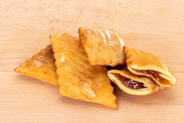 Bugie (Lies) or frappe or chiacchiere or angel wings.Traditional italian carnival fried dessert filled with orange marmalade, isolated on wooden table, clipping path