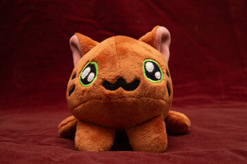 A plush toy cat sewn by hands in golden color lies on a dark red background.