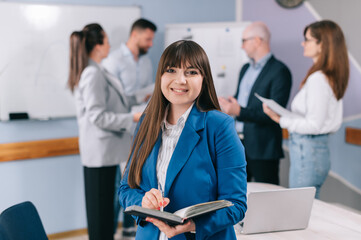 Business woman portrait. Young caucasian woman in a business suit looks at the camera and smiles in the office.