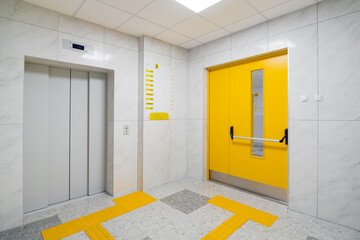 Empty hall with an elevator and yellow double doors, interior of modern hospital or clinic space adapted for handicaps