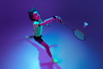 Top view. Portrait of teen boy in uniform playing badminton over blue purple background in neon ligth