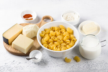 Ingredients for making American pasta: pasta, three types of cheese, cream, butter, flour, spices and salt on a light gray background. Cooking delicious homemade