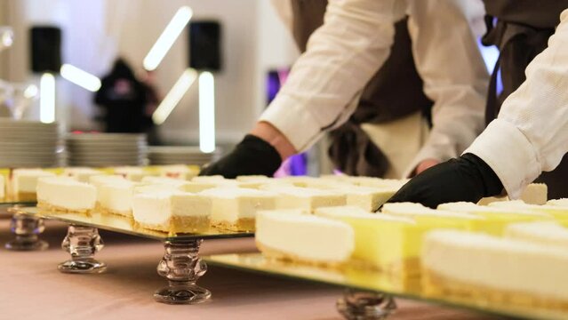A waiter in black gloves puts a mirrored tray of cheesecakes on the table. Slow motion horizontal video