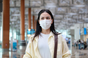Obraz premium A traveller woman is wearing protective mask in International airport, travel under Covid-19 pandemic, safety travels, social distancing protocol, New normal travel concept