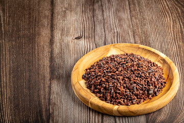 Cocoa nibs on wooden plate.