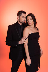 bearded man in black suit seducing brunette woman in dress on pink.