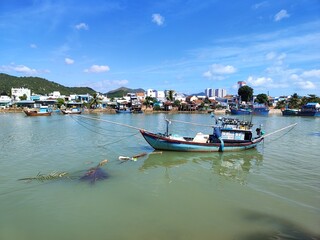 A bright fishing boat on the river against the background of urban slums