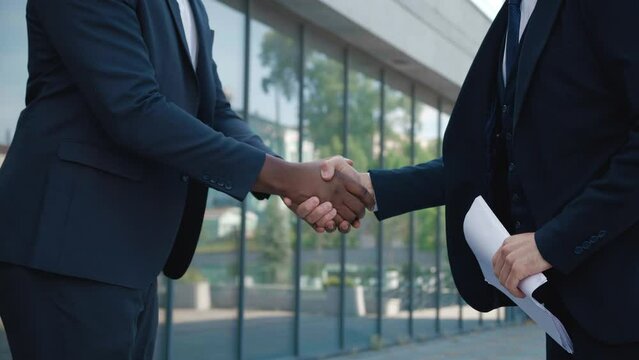 Close up handshake of two male entrepreneurs making win-win deal standing outdoors. Hands of two successful entrepreneurs in business suits shaking hands, standing in downtown near office building