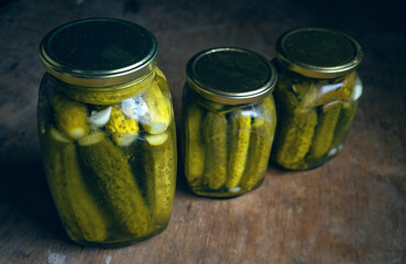 Glass jars with pickled cucumbers on a wooden table. Homemade pickles for the winter. Preservation of cucumbers.