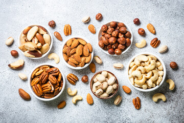 Assortment of nuts in bowls. Cashew, hazelnuts, pecan, almonds, brazilian nuts and pistachios. Top view with at Light stone table.