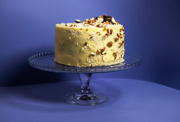 Festive banana cake in white chocolate, decorated with nuts, cookies and chocolate on a purple background. exclusive pastries according to the author's recipes. for a culinary blog and a pastry shop