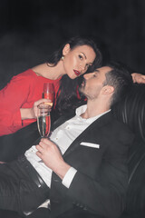 sexy couple in formal wear holding glasses of champagne on black with smoke.