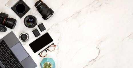 Modern layout of white marble desk of photography with laptop, camera, eyeglasses, smart phone and lenses.