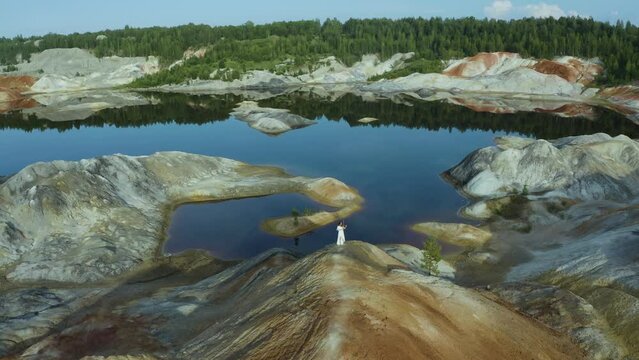 drone camera flies over the quarry mountain where a violinist in white long dress is playing.