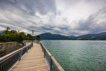 Fototapeta premium At Tegernsee on a slightly rainy summer day. Gray rain clouds move in the sky over the lake, covering the Alps panorama. Clear water of the mountain lake. Tegernsee is a town in Bavaria, Germany