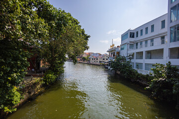 Malacca, Malaysia - August 10, 2022: Along the Melaka river in the old town. Bars and restaurants line the course of the river. Trees line the river bank. The water canal is used by tourist boats - obrazy, fototapety, plakaty
