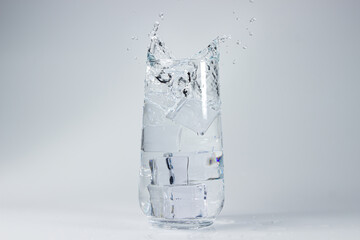 Ice cubes fall into a glass of water on a white background