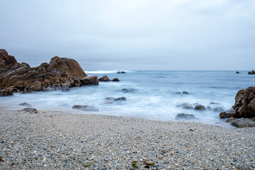 Long exposure motion blur of waves along a rock beach in the Pacific Ocean.