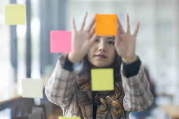Business female employee with many conflicting priorities arranging sticky notes commenting and brainstorming on work priorities colleague in a modern office. 