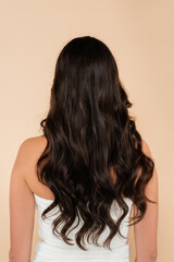Fototapeta premium Back view of woman with wavy hair standing isolated on beige.