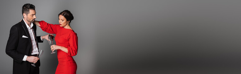 Man in suit pouring champagne in glass of girlfriend on grey background, banner.