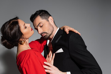 Elegant man touching sensual girlfriend in dress on grey background.