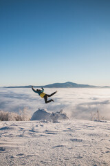 Energetic boy in winter clothes jumping from a stump into the fresh snow with a view of the sunrise and clouds rolling along the mountains