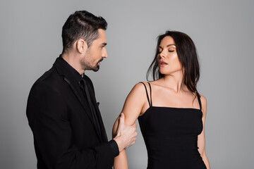 bearded man pulling hand of brunette and sexy woman isolated on grey.